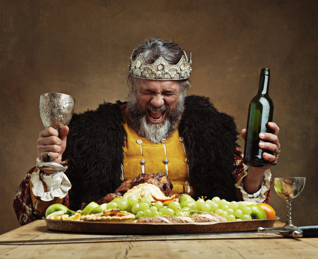 King laughing holding bottle and cup at a table with food
