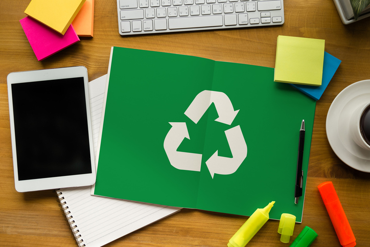Desktop with stationary items on it and a green folder with a recycling symbol on it